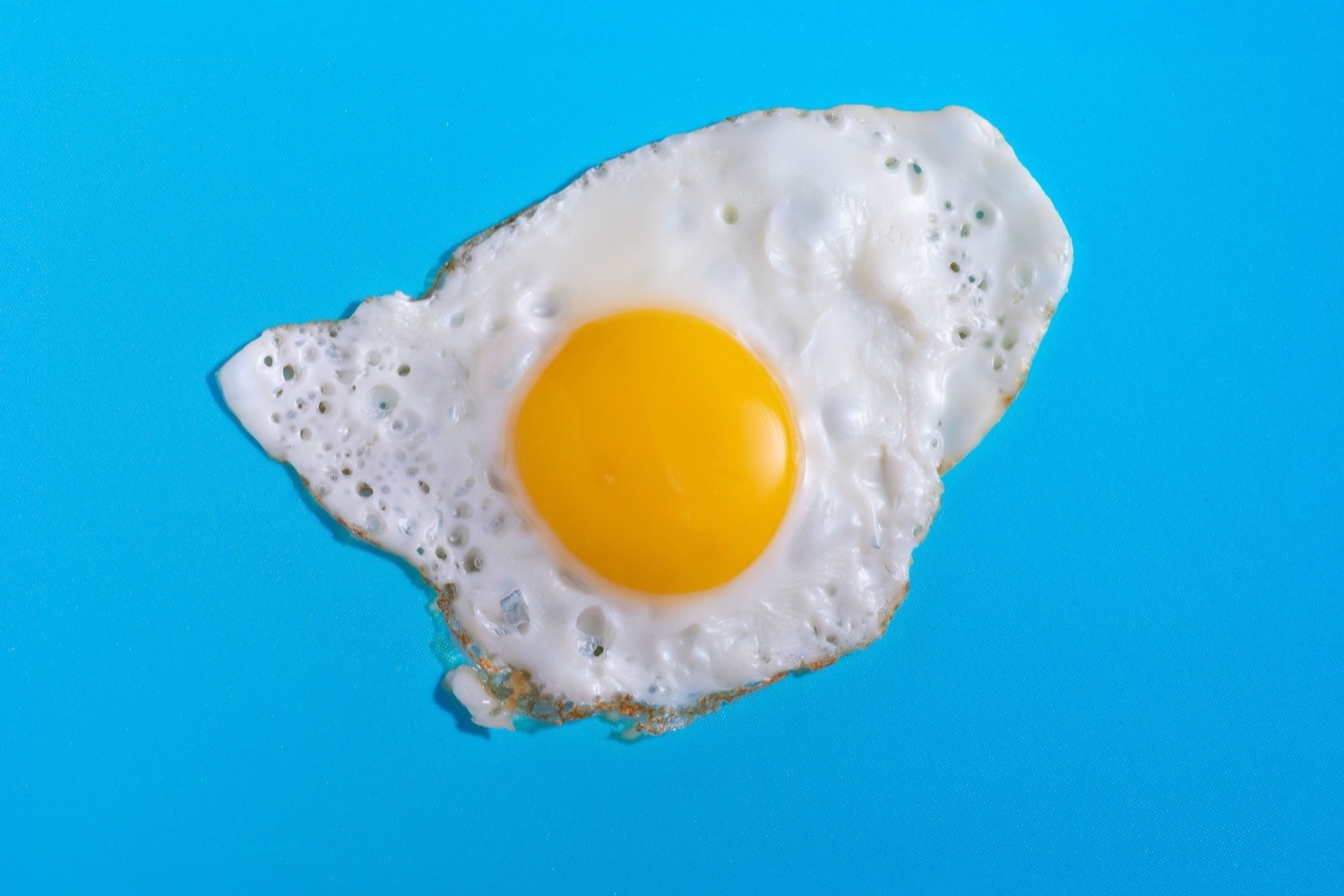 A single fried egg on a flat blue surface.